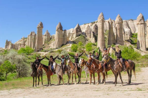 Een groep ruiters juicht te paard tussen de rotspieken van Cappadocië